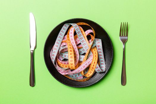 Top view of heap of colorful measuring tapes in plate on green background. Diet concept with copy space.