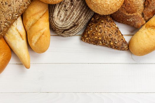 Assortment of baked bread on white wooden table background. top view with copy space.