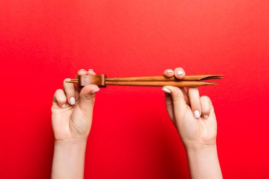 Crop image of two female hands holding chopsticks on red background. Ready to eat concept with copy space.