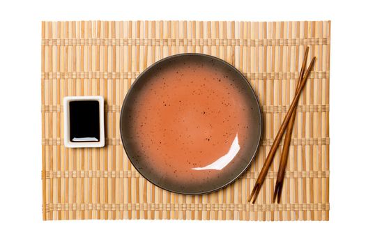 Empty round brown plate with chopsticks for sushi and soy sauce on yellow bamboo mat background. Top view with copy space for you design.