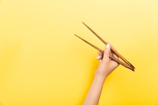 Female hand with chopsticks on yellow background. Traditional asian food with emty space for your design.