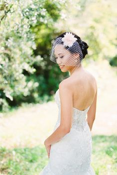 Bride in a white dress and with a veil on her face stands half-turned. High quality photo
