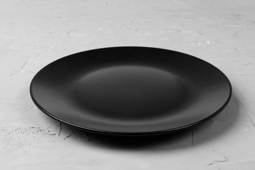 Top view of matte round empty black plate on grey cement background copy space for you design. Perspective view.