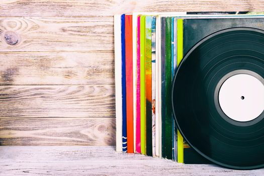 Retro styled image of a collection of old vinyl record lp's with sleeves on a wooden background with Copy space toned.