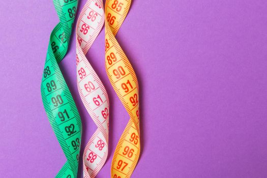 Close up of colorful measure tapes on purple background. Perfect female figure measurements concept.