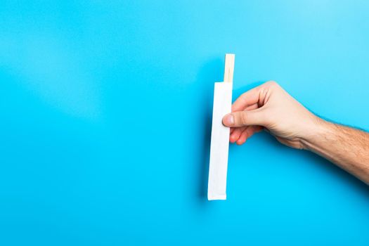 Cropped image of male hand showing chopsticks on blue background. Asian food concept with copy space.