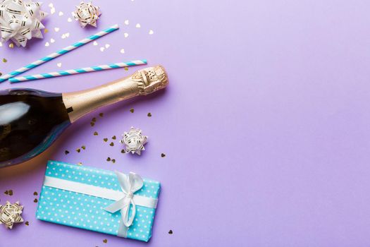 Bottle of champagne with colored glitter, confetti and gift box space for text on colorfull background, top view. Hilarious, christmas and birthday celebration.