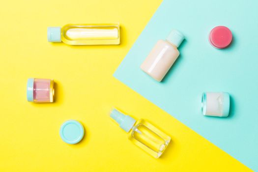 Top view of cosmetic containers, sprays, jars and bottles on yellow and blue background. Close-up view with empty space for your design.