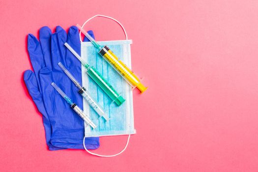 Top view of disposable surgical mask, pair of latex medical gloves and syringe on pink background. Virus protection concept with copy space.