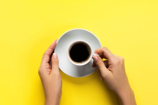 High angle of woman hands holding coffee cup on yellow background Minimalistic style. Flat lay, top view isolated.