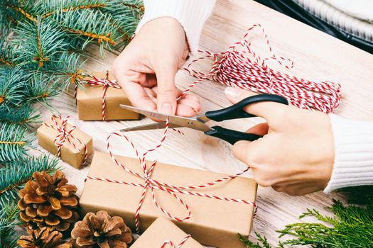 Woman wrapping christmas present , girl prepares xmas gifts with fir tree and pine cone. Hand crafted gift on wooden background with Christmas decor. Top view, copy space. Toned.