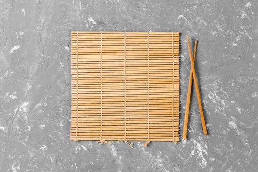 two sushi chopsticks with empty brown bamboo mat or wood plate on cement Background Top view with copy space. empty asian food background.