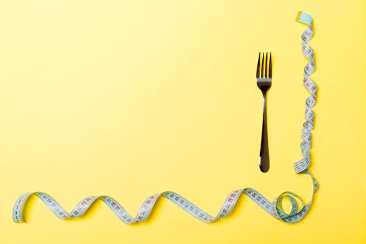 Top view of fork and curled measuring tape on yellow background. Diet concept with copy space.
