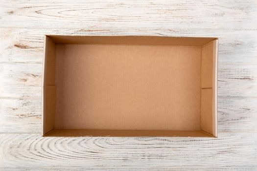 Opened brown blank cardboard box on wooden background, top view.
