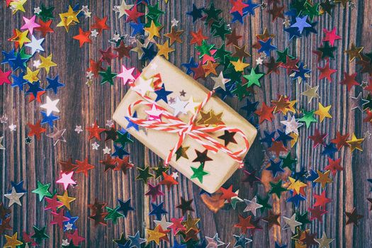 Gift box with star. Creative concept with festive decor on black background. Confetti stars, red, yellow with gift box. Explosion of confetti. Toned.