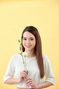 Beauty portrait of lady 20s holding white lisianthus flowers over yellow background