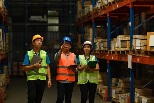 Warehouse workers wearing safety hardhat working on retail warehouse full of packed boxes and goods.