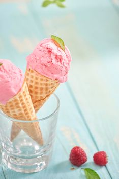 Homemade raspberry ice cream in waffle cones on rustic wooden background, selective focus. Summer time