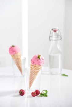 Waffle cone filled with fresh raspberry ice cream in glass cup with fresh raspberry sitting on tabletop