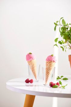 Waffle cone filled with fresh raspberry ice cream in glass cup with fresh raspberry sitting on tabletop