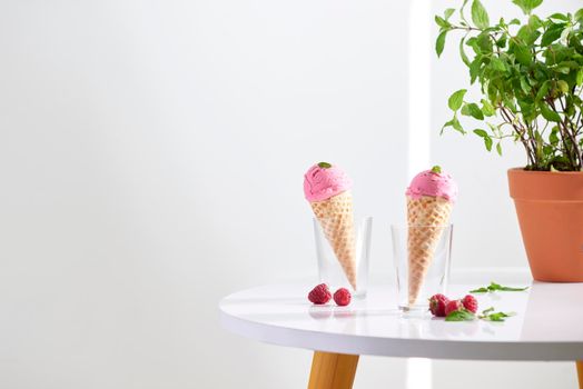 Waffle cone filled with fresh raspberry ice cream in glass cup with fresh raspberry sitting on tabletop