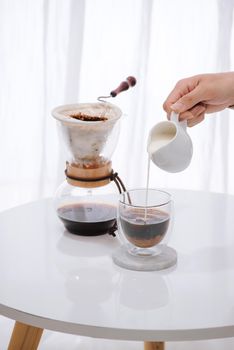 Man pouring milk into glass with cold brew coffee on table