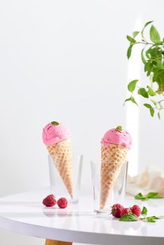 Waffle cone filled with fresh raspberry ice cream in glass cup with fresh raspberry sitting on tabletop