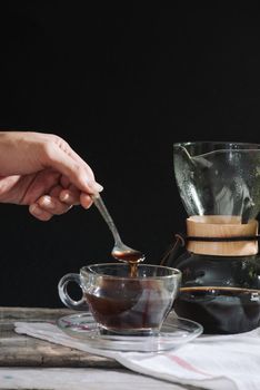 Drip brewing coffee concept. Wooden desk with chocolate cake and cup of coffee on black background. 