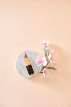 Red lipstick make up and flowers arranged on a pastel purple background with empty space at side