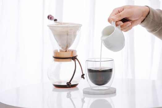 Man pouring milk into glass with cold brew coffee on table