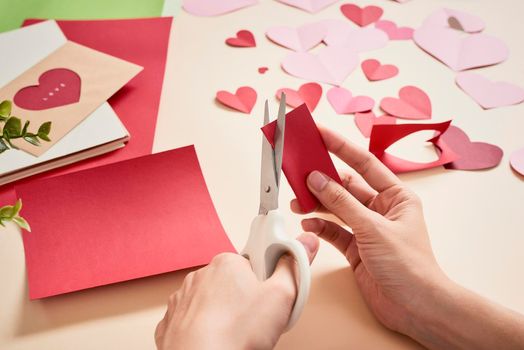 woman cuts out red felt hearts, homemade crafts for Valentine's day, hand made creativity, top view