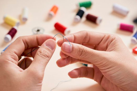 people, needlework, sewing and tailoring concept - tailor woman with thread in needle stitching fabric. Hands sewing with a needle and thread. Fingers pulling thread into the needle