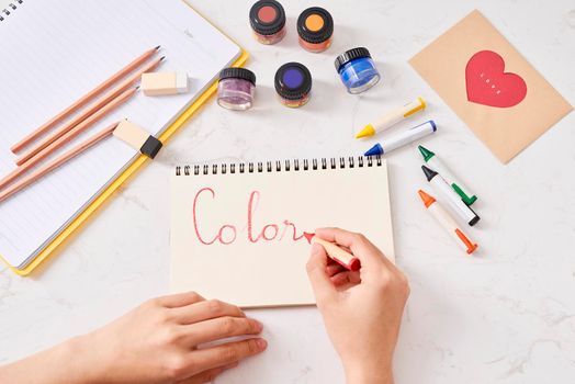 Hand with color pencils and blank sheet of paper on white table