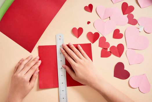 woman cuts out red felt hearts, homemade crafts for Valentine's day, hand made creativity, top view