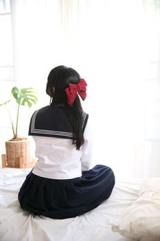 japanese school girl sitting on bedroom in white tone 