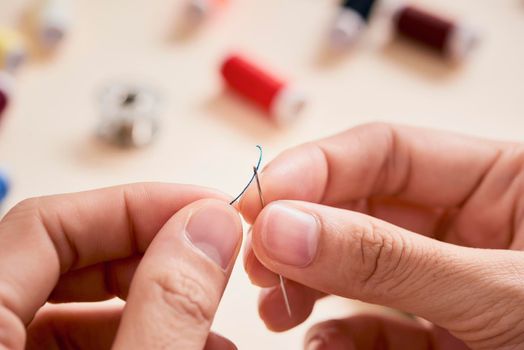 people, needlework, sewing and tailoring concept - tailor woman with thread in needle stitching fabric. Hands sewing with a needle and thread. Fingers pulling thread into the needle