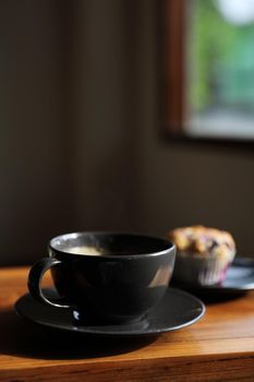 Coffee cup with muffin on wood table in local coffee shop