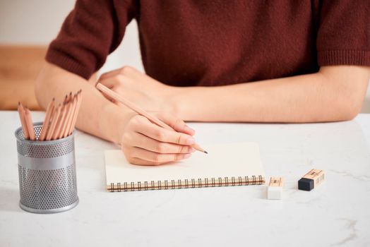 Hand with color pencils and blank sheet of paper on white table