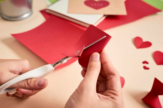 woman cuts out red felt hearts, homemade crafts for Valentine's day, hand made creativity, top view