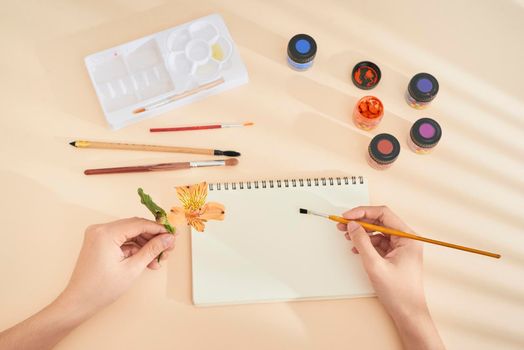 women's hand with brush drawing on notepad. Creation process of watercolor painting