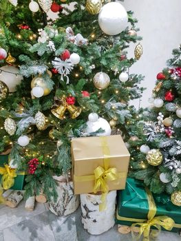 Beautiful boxes wrapped in gold paper with Christmas gifts on a birch stump near the Christmas tree in the room.