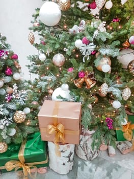 Beautiful boxes wrapped in gold paper with Christmas gifts on a birch stump near the Christmas tree in the room.