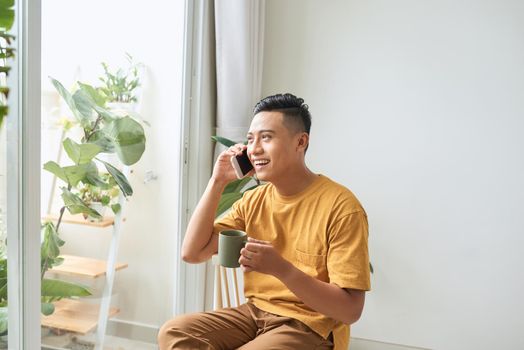 Young man wearing casual clothes talking on a mobile phone in the morning at a window