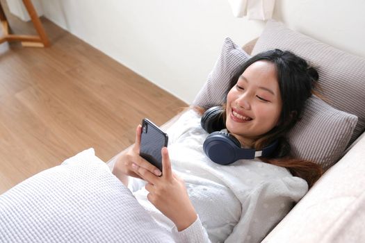 Female lying leaning on comfortable sofa and using her modern mobile phone to chat with her friends, scroll on shopping application or social media