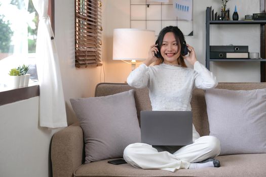 Relaxation lifestyle concept, Young Asian woman is wearing headphone and watching movie on laptop..