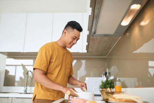 happy young man cutting vegetables in kitchen