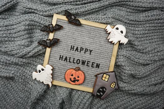 The text is written in the frame - Happy Halloween and there are gingerbread cookies. Gingerbread cookies for Halloween. Knitted gray background for Halloween.