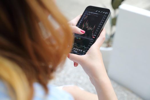 Female hand with smartphone trading stocks online in coffee shop Business concept