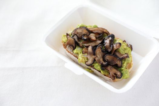 Toast with avocado and grilled mushroom with delivery package in white background