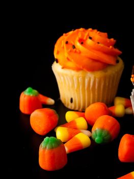 Halloween orange and black cupcakes with candy corn candies on black background.